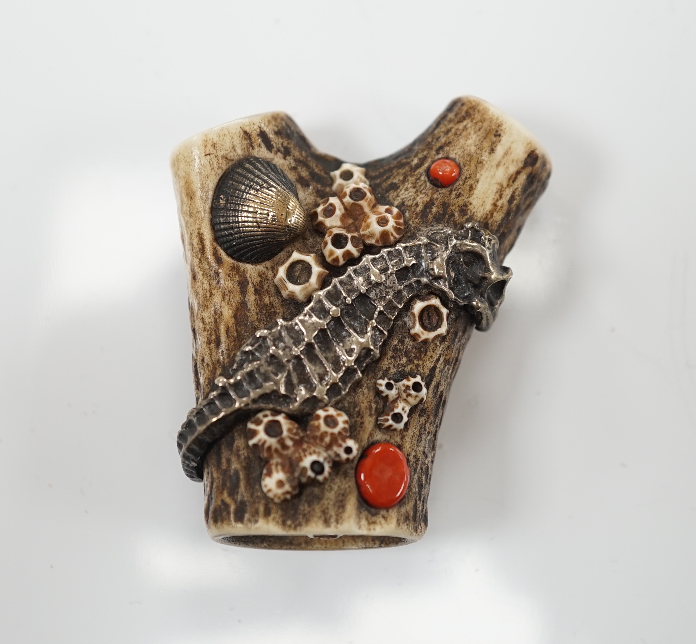 A Japanese coral and mixed metal mounted stag antler netsuke, 19th century, the antler carved in imitation of rocks applied with a white metal seahorse, gilt metal scallop shell, carved bone barnacles, the underside holl